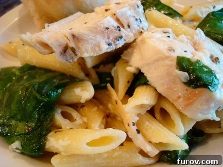 Garlicky Chicken & Fresh Spinach Pasta 2 A close-up shot of a serving of garlic chicken pasta with spinach, showing tender chicken pieces, vibrant green spinach, and pasta coated in a light sauce.