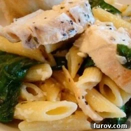 Close up of a serving of Garlic Chicken Pasta with Spinach in a white bowl.