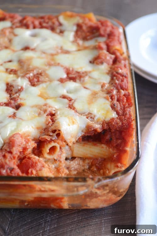 Comforting Baked Ziti Supreme 2 A glass baking dish filled with Classic Baked Ziti, with a serving spoon removing a portion, showing melted cheese and rich tomato sauce.