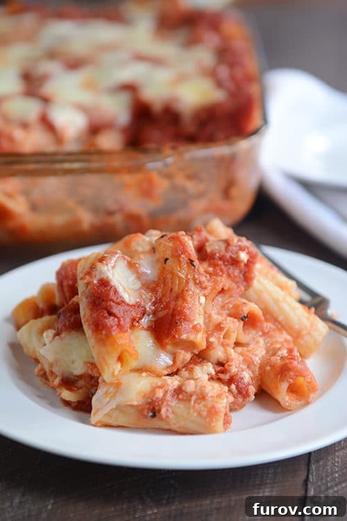 Comforting Baked Ziti Supreme 4 A close-up shot of a scoop of baked ziti on a white plate, revealing tender pasta coated in rich red sauce and strands of gooey melted mozzarella cheese.