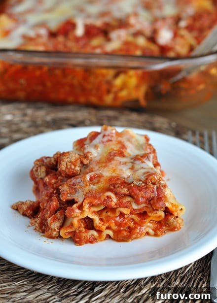 A white plate with a perfectly portioned helping of red lasagna roll.