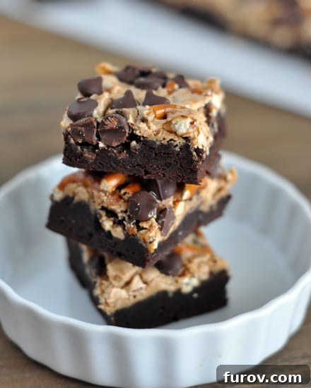 Three pretzel and chocolate chip topped brownies stacked on top of each other in a white ramekin.