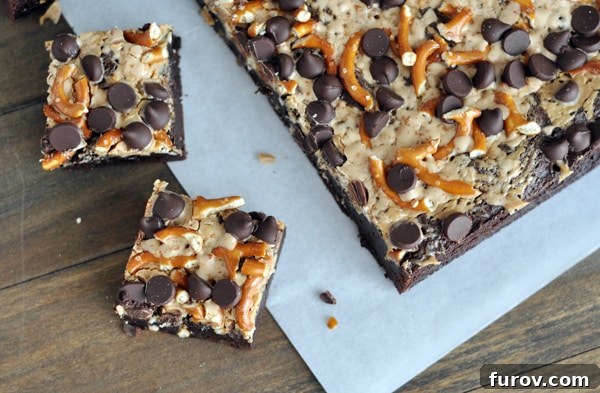 Top view of a slab of pretzel and chocolate chip topped brownies with two brownies cut off the slab on the side.