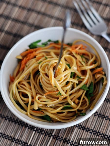 A beautifully arranged white bowl of cooked spicy Thai linguine noodles, garnished with fresh herbs and chopped peanuts, presented from a top-down perspective.