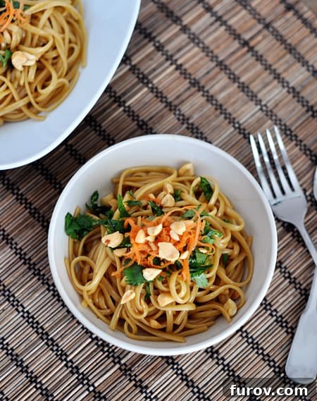 A vibrant aerial shot of super simple spicy Thai noodles in a white bowl, adorned with fresh cilantro, green onions, and finely chopped peanuts, ready to be enjoyed.