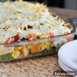 Layered Mexican Cornbread Salad in a glass dish with a serving spoon.