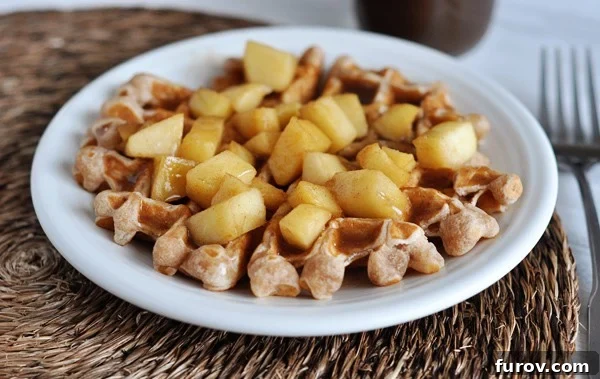 Warm Spiced Apple Waffles with Cinnamon Drizzle 2 White plate with a waffle covered in apple chunks and a cinnamon sauce, ready to be enjoyed.
