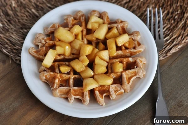 Warm Spiced Apple Waffles with Cinnamon Drizzle 4 Top view of a waffle on a white plate covered in cooked apples and cinnamon, garnished beautifully.