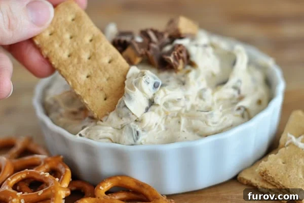 A white bowl full of creamy peanut butter cookie dough dip with a graham cracker perfectly dipped into it, ready to be enjoyed.