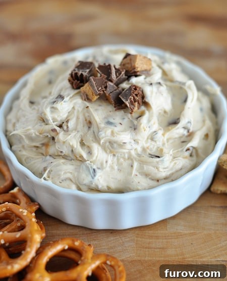 Close-up top view of a white bowl filled with creamy peanut butter dip, generously topped with chopped peanut butter cups and chocolate chips.