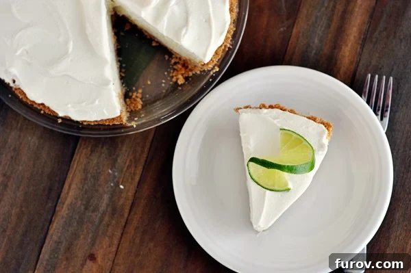 Top view of a slice of sour cream lime tart on a white plate with a slice of lime on top, showcasing its vibrant color and smooth texture.
