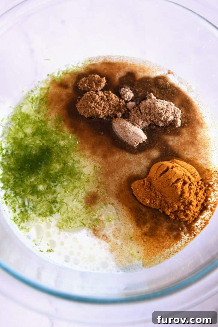 Glass bowl filled with the base ingredients for the marinade: coconut milk, vibrant lime zest, golden curry powder, fragrant coriander, and earthy cumin.