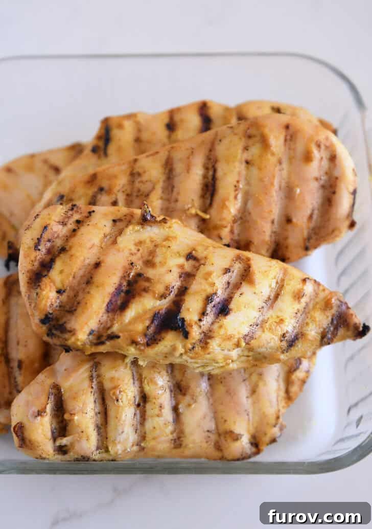 Beautifully grilled chicken breasts, golden and tender, arranged in a clear glass dish, awaiting their final drizzle of sauce.