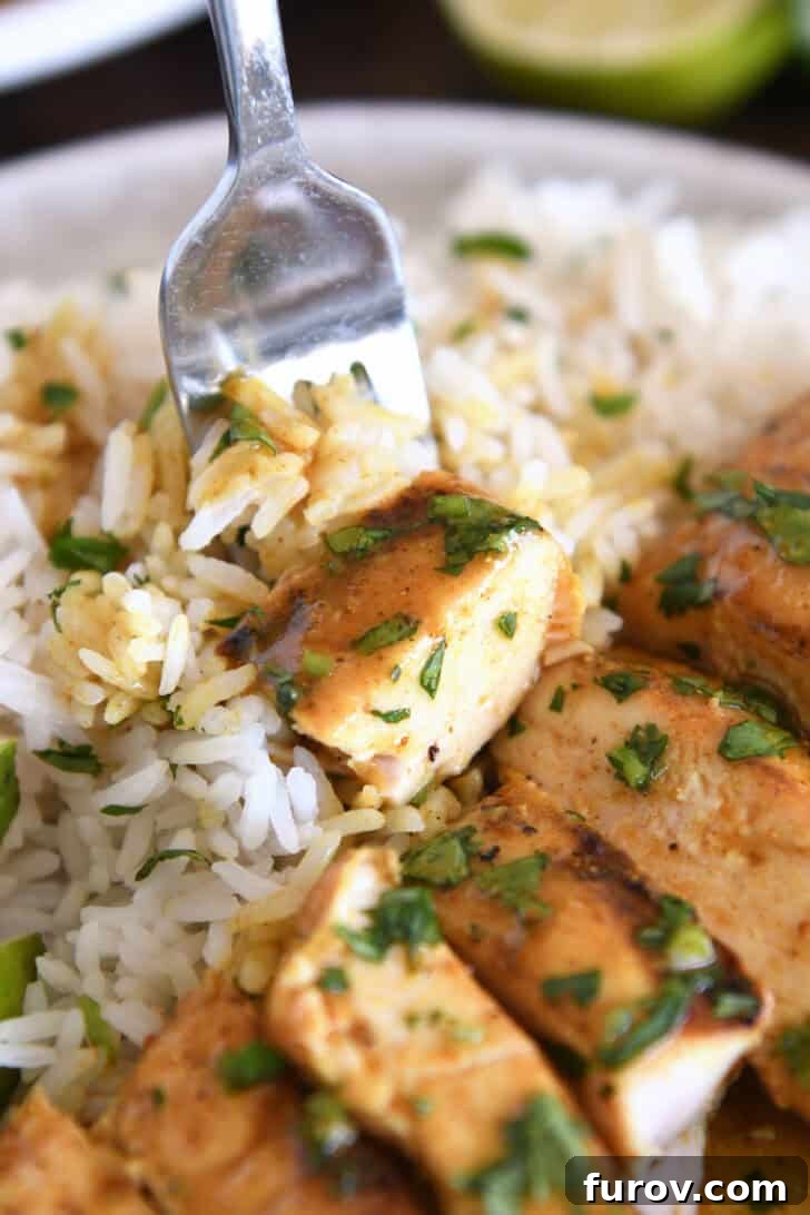 A succulent piece of grilled chicken on a fork, poised above a bed of fluffy rice and garnished with fresh cilantro, inviting a delicious bite.