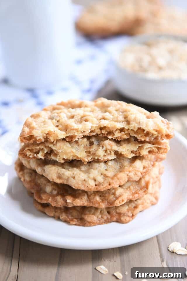 Crisp Oatmeal Thins 5 Four thin oatmeal cookies on a white plate with the top cookie broken in half, highlighting its crisp interior.
