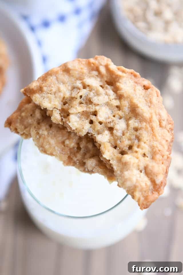 Crisp Oatmeal Thins 6 Two thin oatmeal cookie halves delicately balanced on the rim of a glass of cold milk.