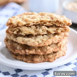 Four crispy oatmeal cookies stacked on a white plate, emphasizing their thinness.
