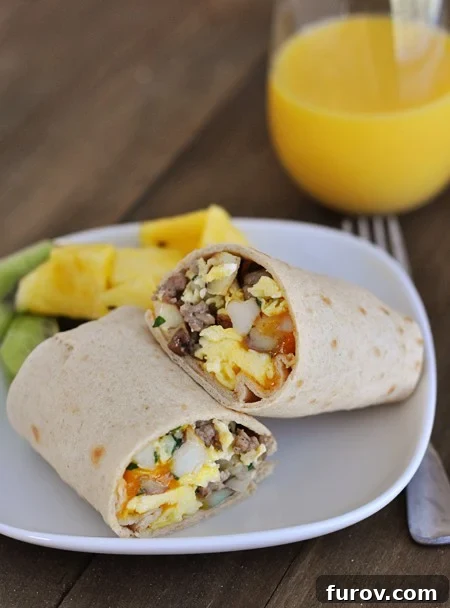 Morning Fuel Wraps 2 A breakfast burrito cut in half on a white plate next to fresh fruit, showcasing the rich filling.