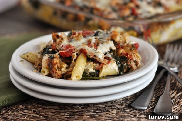 A generous serving of Pesto Sausage Baked Ziti beautifully arranged on a white plate, part of a stack of three.