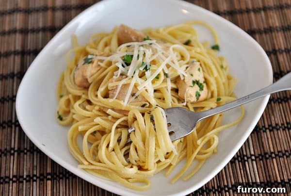 A fork twirling a bite of chicken linguine on a white plate, showcasing the delicious strands of pasta.