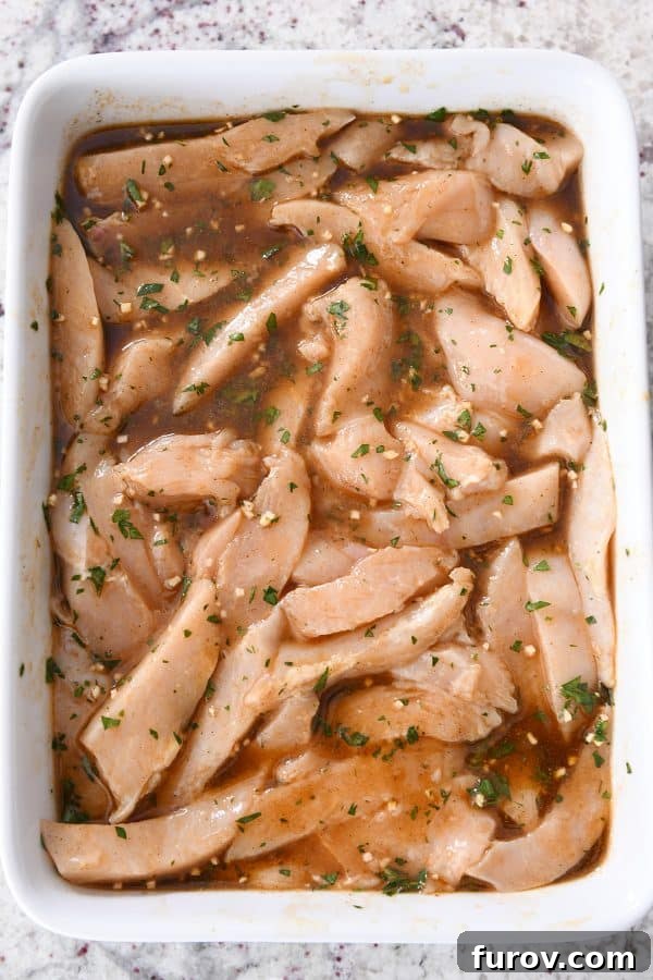 Chicken strips marinating in white dish, soaking up the rich, vibrant flavors of the marinade.