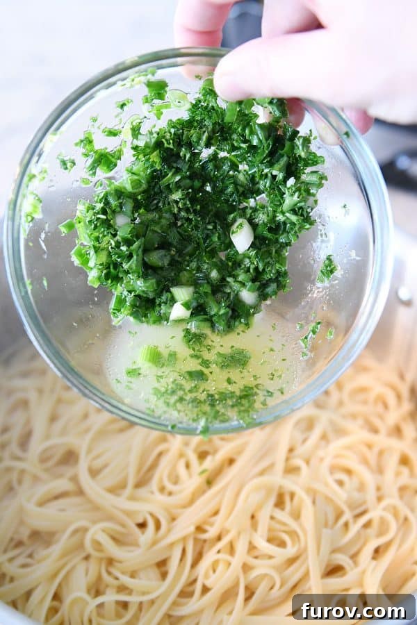 Adding fresh green onions and lemon juice to cooked linguine in a large bowl, highlighting the vibrant colors and fresh ingredients.