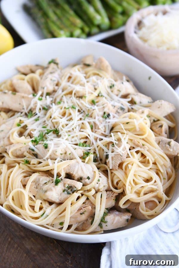 Tossed lemon chicken pasta in white bowl with Parmesan cheese and fresh parsley, presented beautifully for serving.