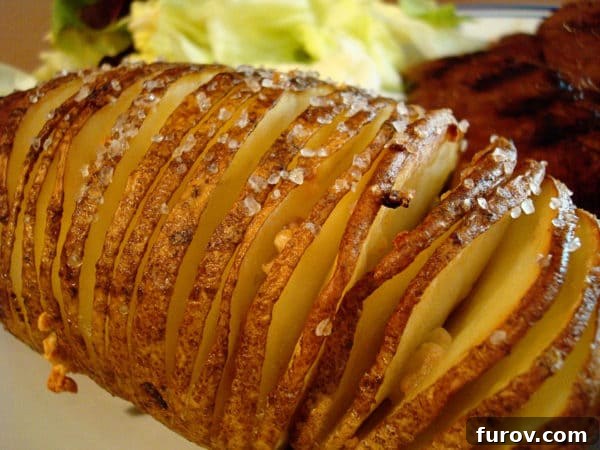 A raw baking potato intricately sliced into thin, accordion-like segments, ready for seasoning and baking.