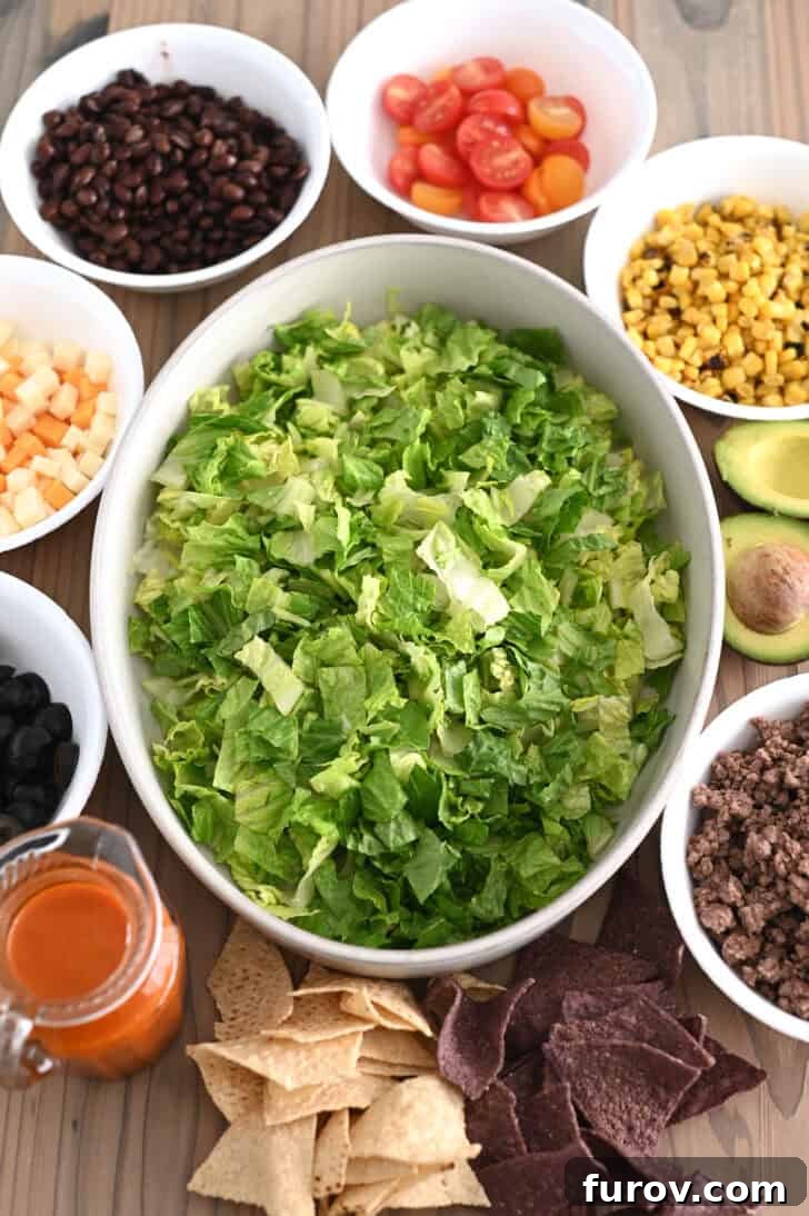Zesty Chopped Taco Salad with Homemade Catalina 3 Bowl of lettuce in the center with bowls of black beans, chopped tomatoes, roasted corn, cubed cheese, avocados, and cooked ground beef on the side, ready for assembly.