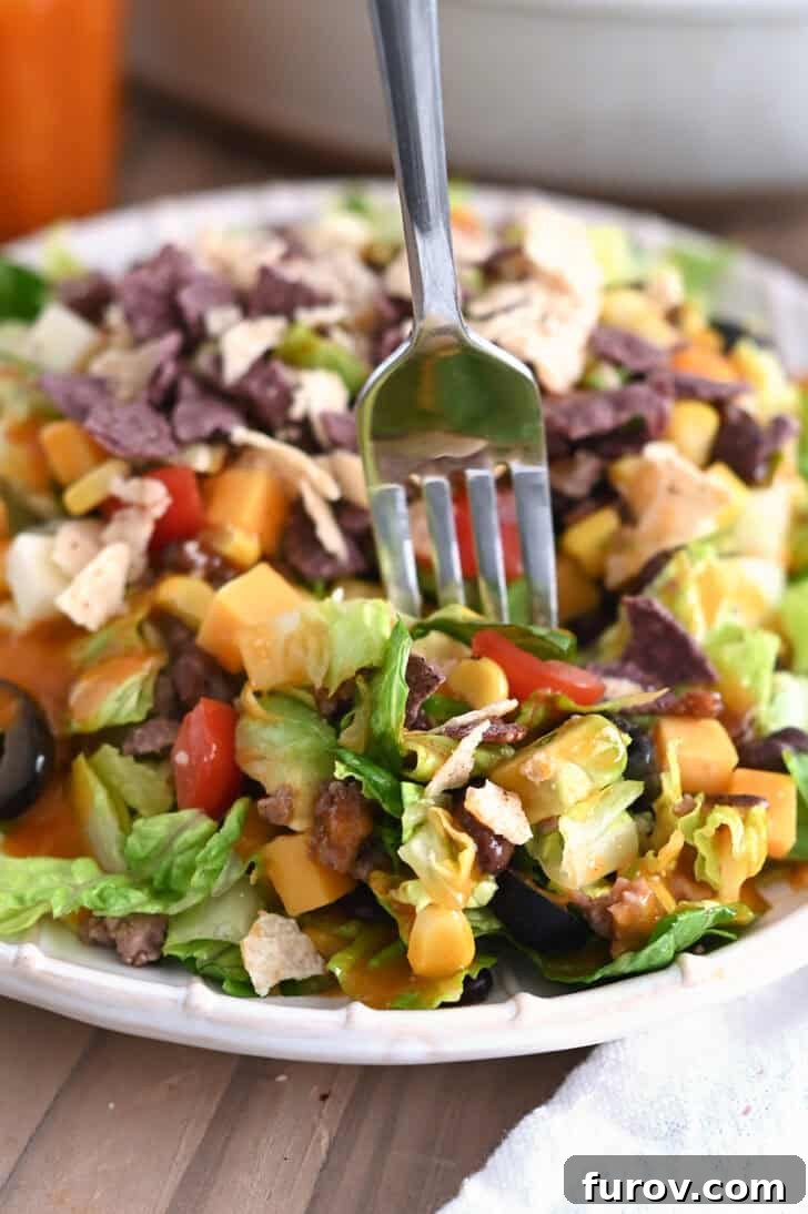 Zesty Chopped Taco Salad with Homemade Catalina 7 Fork scooping a delicious bite of chopped taco salad on a white ridged plate.