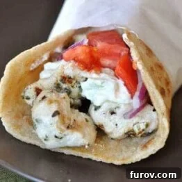 Wrapped chicken gyro on a black plate.