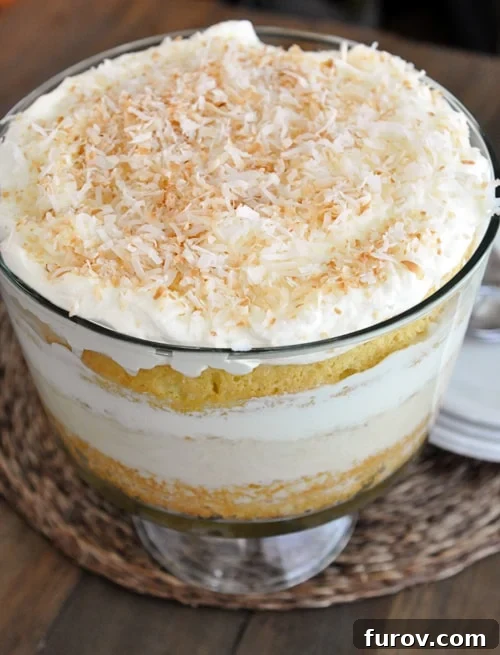 Decadent Coconut Tres Leches Trifle 4 A close-up shot of a Coconut Tres Leches Cake Trifle in a clear glass dish, highlighting the distinct layers of cake, creams, and toasted coconut.