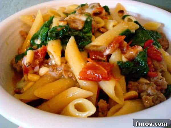A beautifully plated bowl of penne pasta, generously mixed with savory sausage, wilted spinach, and vibrant sun-dried tomatoes. A perfect representation of a hearty and delicious skillet supper.
