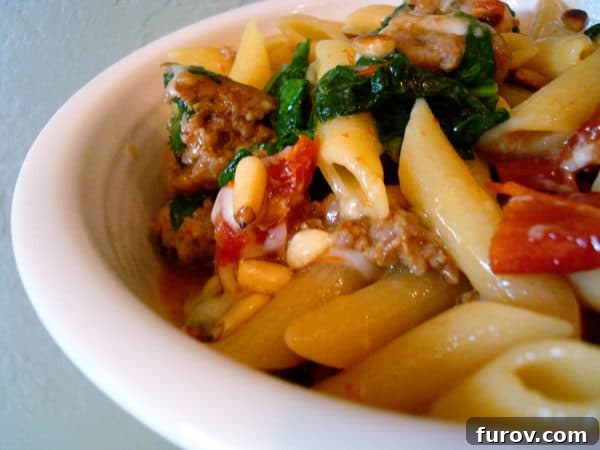 Close-up shot of a white bowl overflowing with the Sausage and Spinach Penne Skillet Supper, showcasing the chunky sausage, bright green spinach, and deep red sun-dried tomatoes intertwined with the penne pasta.
