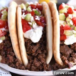 Front view of three stuffed Greek flatbread tacos, generously topped with creamy tzatziki sauce, crisp chopped cucumbers, and vibrant diced tomatoes.