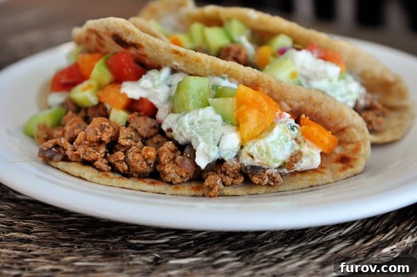 Olympian Taco Feast 5 Two perfectly stuffed Greek tacos resting on a crisp white plate, highlighting their vibrant fillings and appealing presentation.