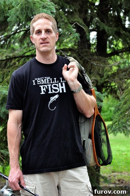 man wearing a black t-shirt that proudly declares 'I'm happy when I smell like fish' while holding fishing gear