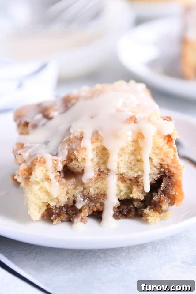 Square of cinnamon cake with glaze drizzling down sides.