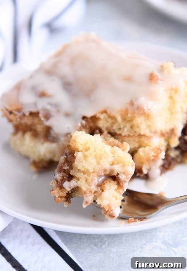 Bite of cinnamon roll cake on fork on white plate.