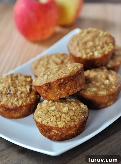 A beautiful white platter showcasing a generous selection of freshly baked healthy applesauce oat muffins, beautifully studded with oats. In the background, fresh apples hint at the natural sweetness within.