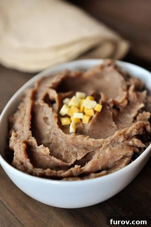 White oval dish full of refried beans topped with small cheese cubes.