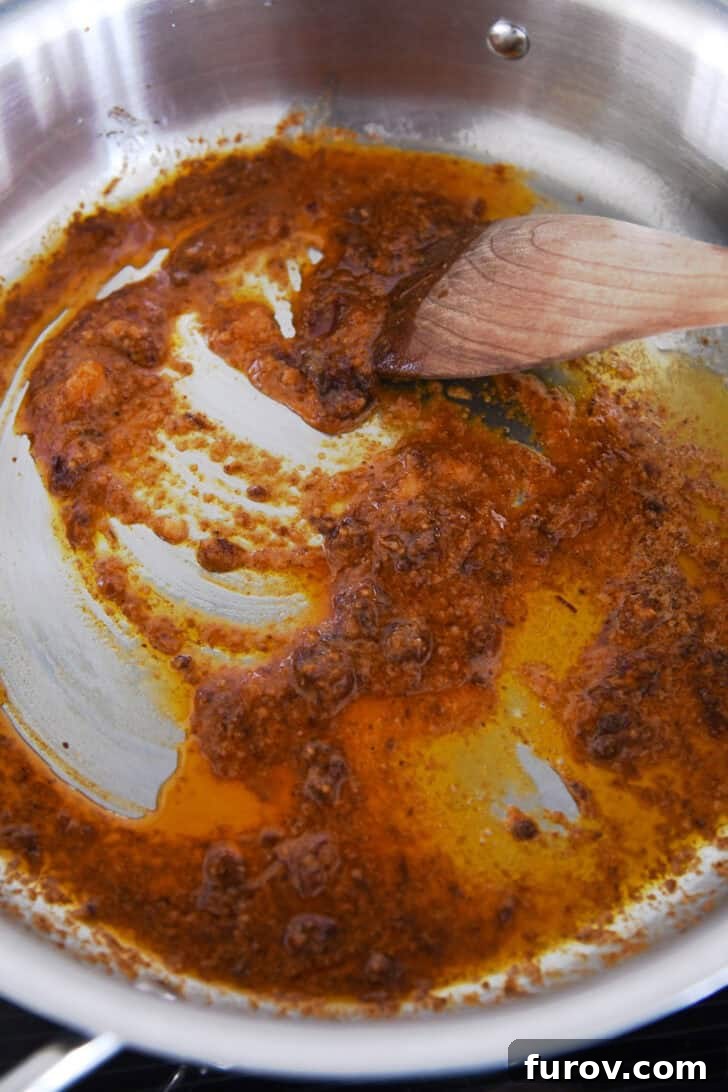 A wooden spoon stirring a chipotle, garlic, and oil mixture in a metal pot.