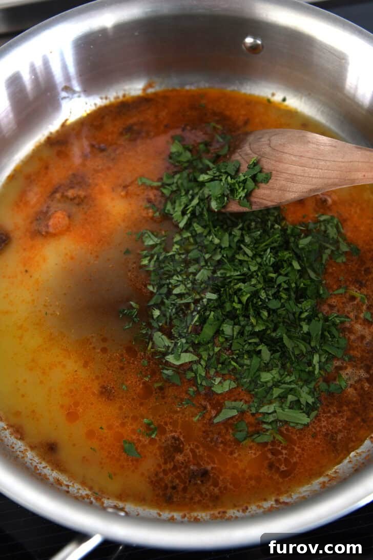 Top down view of a metal pot with an orange chipotle sauce, chopped cilantro, and a wooden spoon about to stir it.
