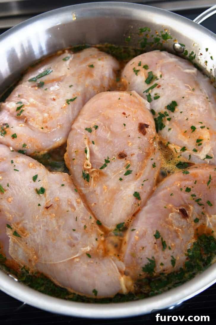 Top down view of raw chicken cooking in a dark cilantro sauce in a metal pot.