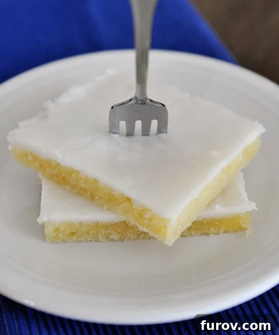 Two pieces of white Texas sheet cake stacked on top of each other with a fork stuck in the top piece.