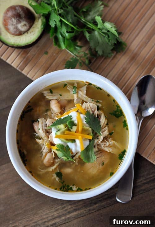 Top-down view of a white bowl overflowing with white bean chicken chili, garnished with fresh parsley leaves and a swirl of sour cream, ready to be enjoyed.