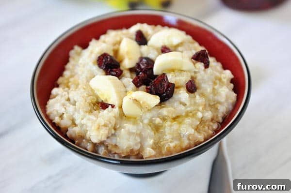 A beautifully presented bowl of cooked steel cut oats, garnished with vibrant banana slices and ruby-red dried cranberries, ready to be enjoyed.
