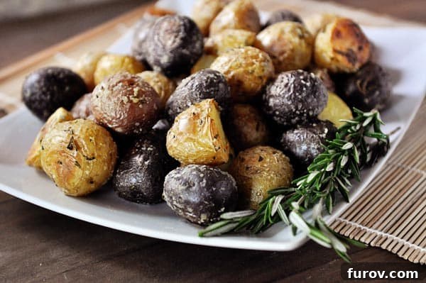A white platter showcasing small, perfectly cooked salt-crusted potatoes with a sprig of fresh rosemary on the side, ready to be served.