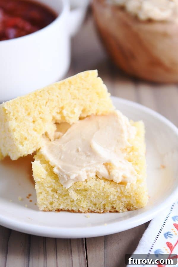 A golden slice of cornbread cut in half, revealing its fluffy interior, served with creamy, fluffy honey butter.