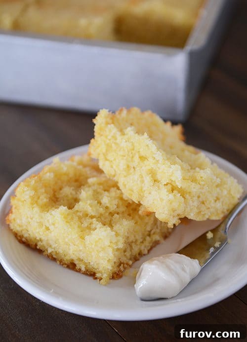A white plate featuring a split piece of cornbread, a spreading knife, and a dollop of butter on the side.